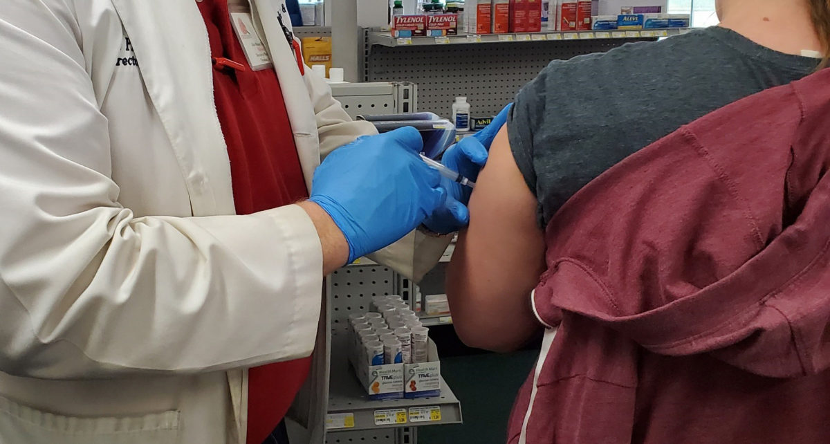 Dale wearing blue gloves giving a flu shot to a patient.