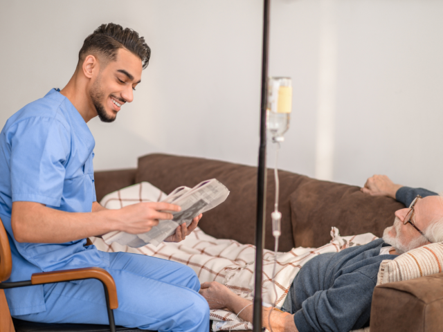A male patient laying on the couch receiving Ig therapy with a nurse reading to him