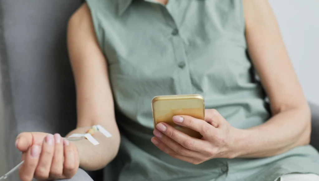 Woman scrolling on her phone receiving immunoglobulin therapy.